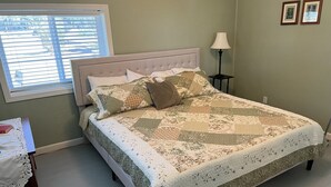 A neatly made bed with a patterned quilt, a bedside table with a book, and a lamp on a nightstand.