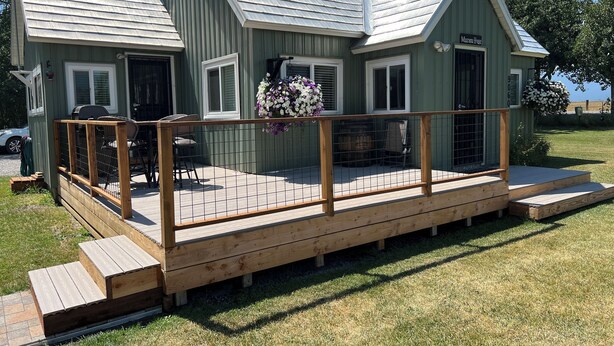 A small, single-story house with a porch and a deck, featuring a metal roof and a sign that reads "Mazama House."