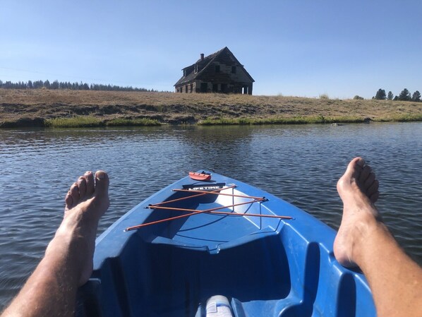 Kayak con los pies de una persona encima, frente a una casa junto a aguas tranquilas.