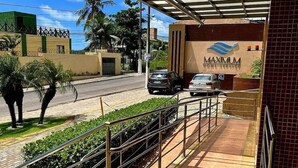 Entrada de un hotel con un paseo techado, palmeras y cielo despejado.