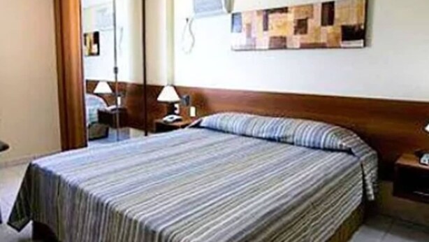 Una habitación de hotel con una cama, una mesita de noche con lámpara, un espejo y un aire acondicionado instalado en la pared.