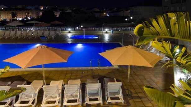 A nighttime pool area with lounge chairs and umbrellas, surrounded by buildings. - Esperanza del Mar Apartments (Sanxenxo)
