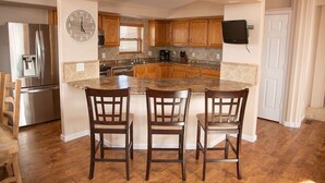 A kitchen with a central island, wooden cabinets, a stainless steel refrigerator, and a wall-mounted TV.