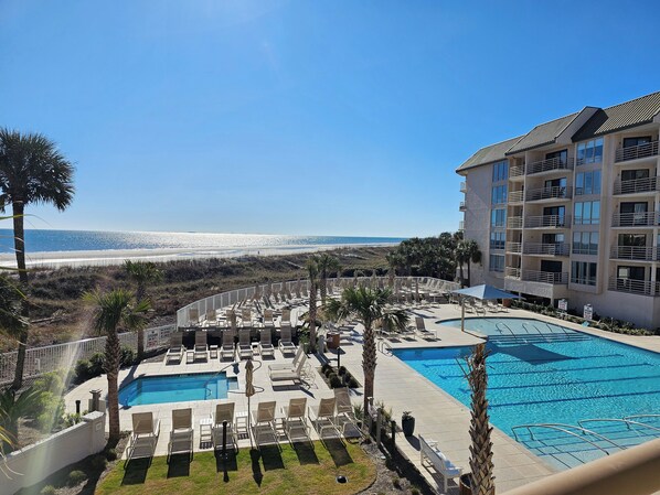 A resort with a pool area, lounge chairs, and a view of the beach.