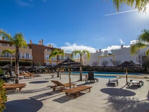 A resort pool area with sun loungers, umbrellas, and a swimming pool.