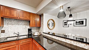 Una cucina moderna con mobili in legno, un piano di lavoro nero, uno schienale piastrellato, uno specchio rotondo e luci a sospensione.