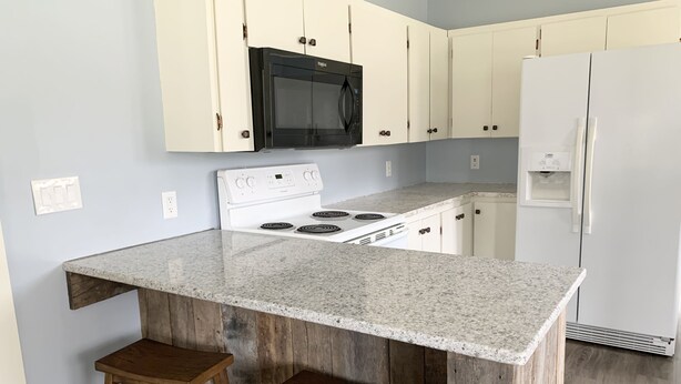 A kitchen with a granite countertop, white cabinets, a black microwave, a white stove, and a white refrigerator. There are two wooden stools at the island. - Family Getaway, Minutes away from Leland, Lake Leelanau, Suttons Bay (Lake Leelanau)