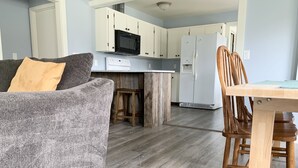 A modern kitchen with white cabinets, a microwave, and a refrigerator. There is a wooden dining table with chairs. - Family Getaway, Minutes away from Leland, Lake Leelanau, Suttons Bay (Lake Leelanau)
