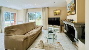 Una sala de estar con sofá, televisión, chimenea y un ventanal con cortinas.