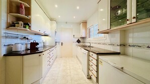 Una cocina estrecha con armarios blancos, una encimera y suelo de baldosas.