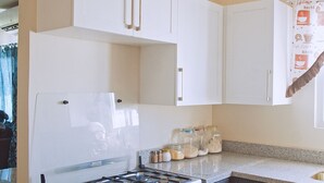 Une cuisine avec des armoires blanches, un évier en acier inoxydable et une cuisinière à gaz. On peut voir des bocaux fermés par des couvercles sur le comptoir.