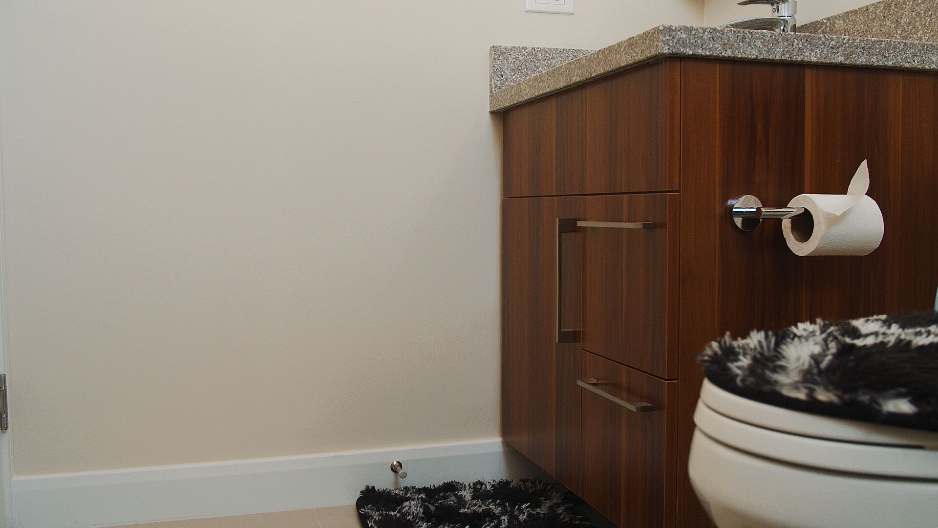 Une salle de bain avec un meuble en bois, des toilettes et un rouleau de papier toilette posé sur un porte-rouleau.