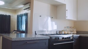 Une cuisine compacte équipée d’une cuisinière, d’un four et d’un plan de travail. On y trouve des bocaux sur le plan de travail et une fenêtre avec des rideaux.