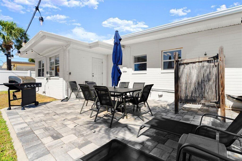 A patio with a table and chairs, a grill, and a blue umbrella.