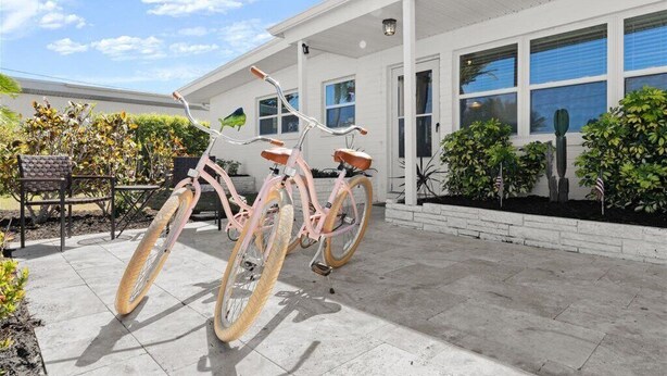 Een fiets geparkeerd voor een wit gebouw met grote ramen en een patio met planten en tuinmeubilair.