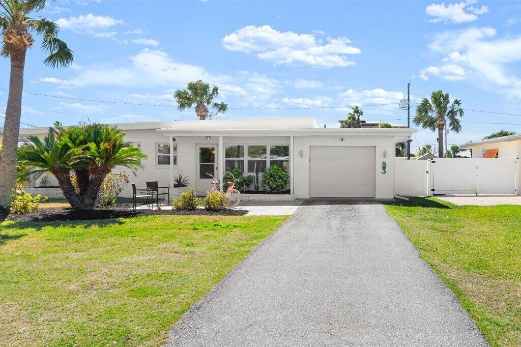 A single-story house with a garage, a paved driveway, and a small front yard with palm trees and shrubs.