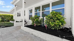 Een wit huis met een overdekte veranda, grote ramen en een tuin met diverse planten.