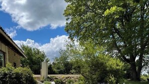 A garden pathway leading to a house with a stone wall and a large tree. - Spacious gite with large heated private swimming pool and new hot tub. (Salerm)