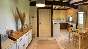 A rustic kitchen with wooden cabinets, a dining table set for four, and a stone wall backdrop. - Spacious gite with large heated private swimming pool and new hot tub. (Salerm)