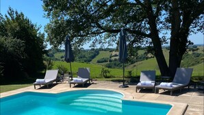A clear blue swimming pool with lounge chairs and umbrellas, surrounded by a landscaped garden and hills in the background. - Spacious gite with large heated private swimming pool and new hot tub. (Salerm)