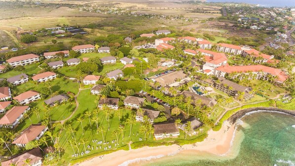 An aerial view of a resort with multiple buildings, a beach, and clear waters.