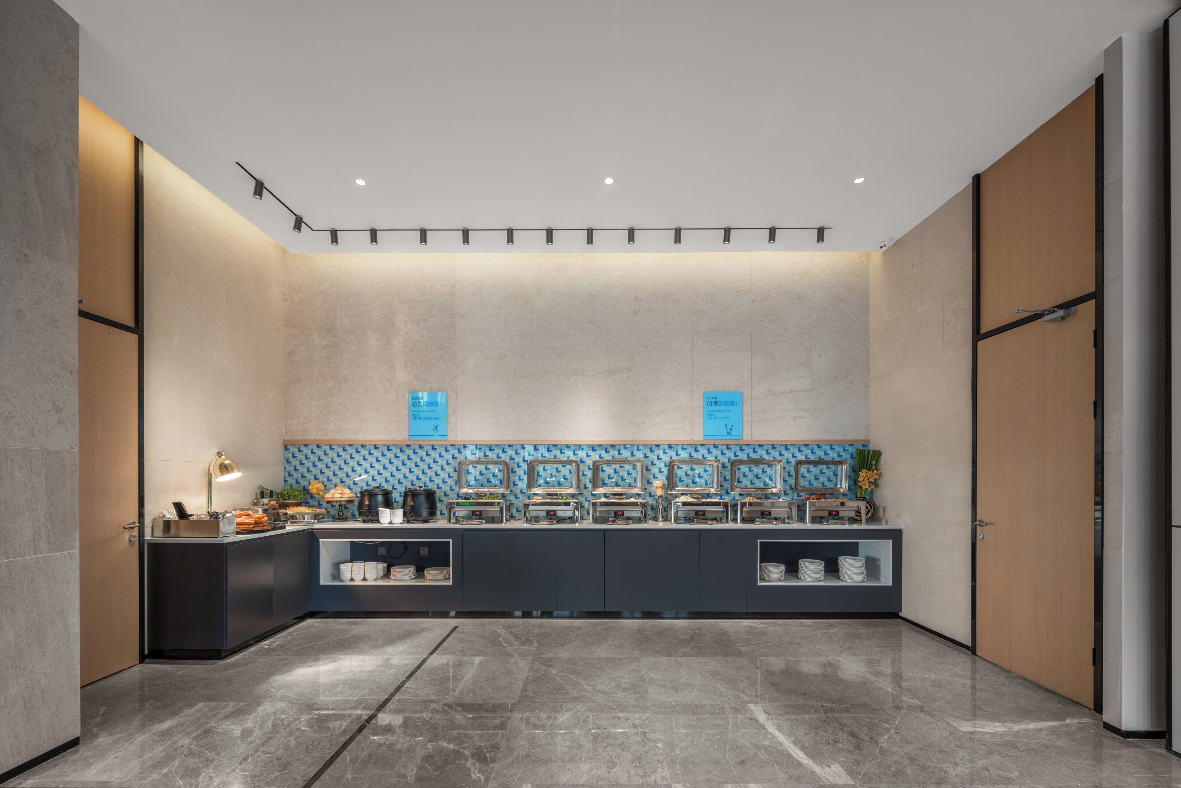 A modern hotel lobby with a marble floor, a reception desk, and a buffet area.
