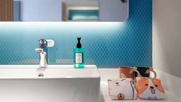 Une salle de bain avec un lavabo blanc, un flacon de savon liquide bleu et deux sacs décorés avec des motifs d’animaux, posés sur le comptoir.