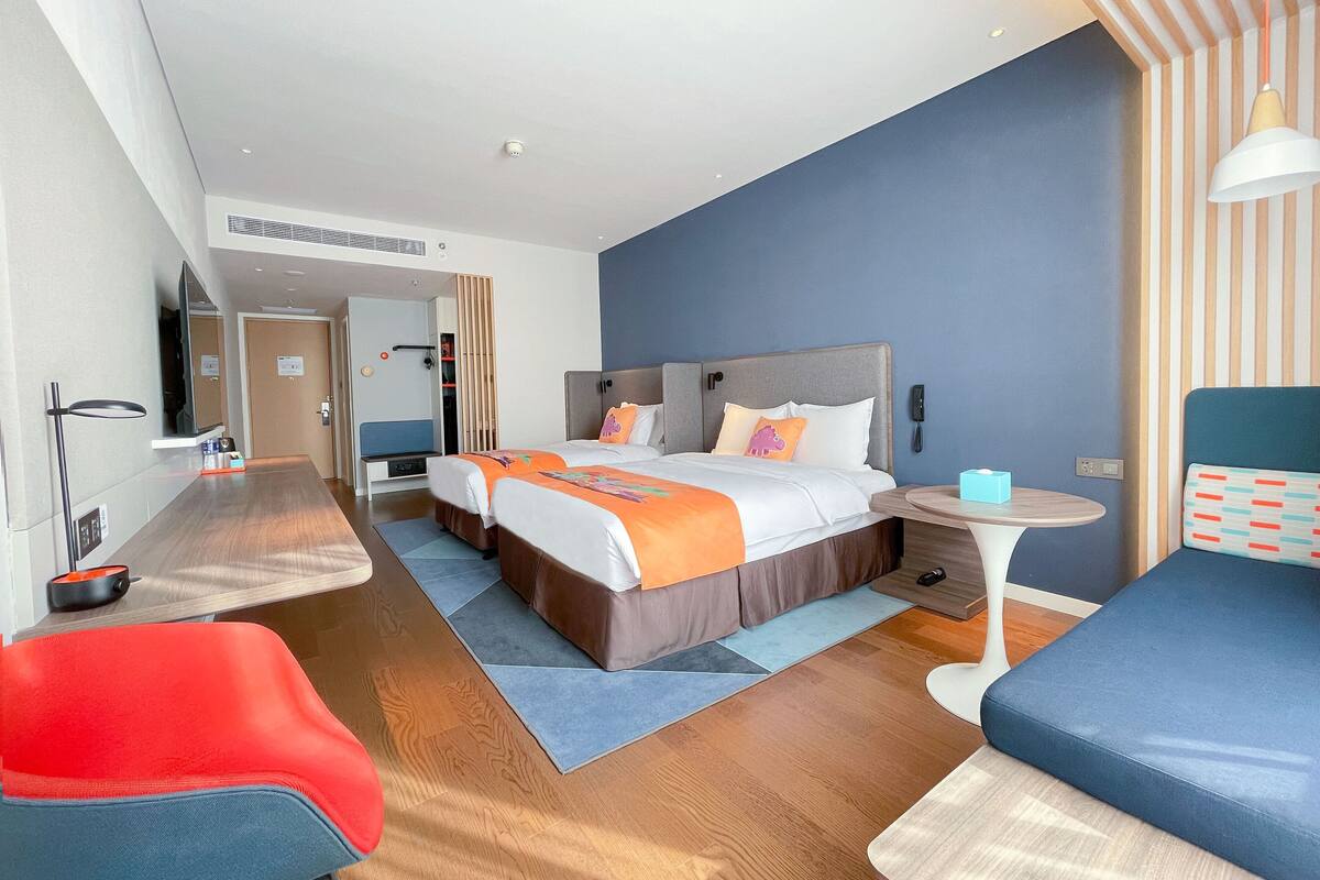 A modern hotel room with a large bed, a desk, a chair, and a small table.