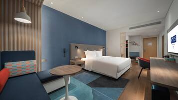 A modern hotel room with a bed, a desk, a chair, and a TV.