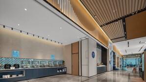 A modern hotel lobby with a long reception desk, a large refrigerator, and a seating area with blue chairs. - Holiday Inn Express Yixing by IHG (Wuxi)