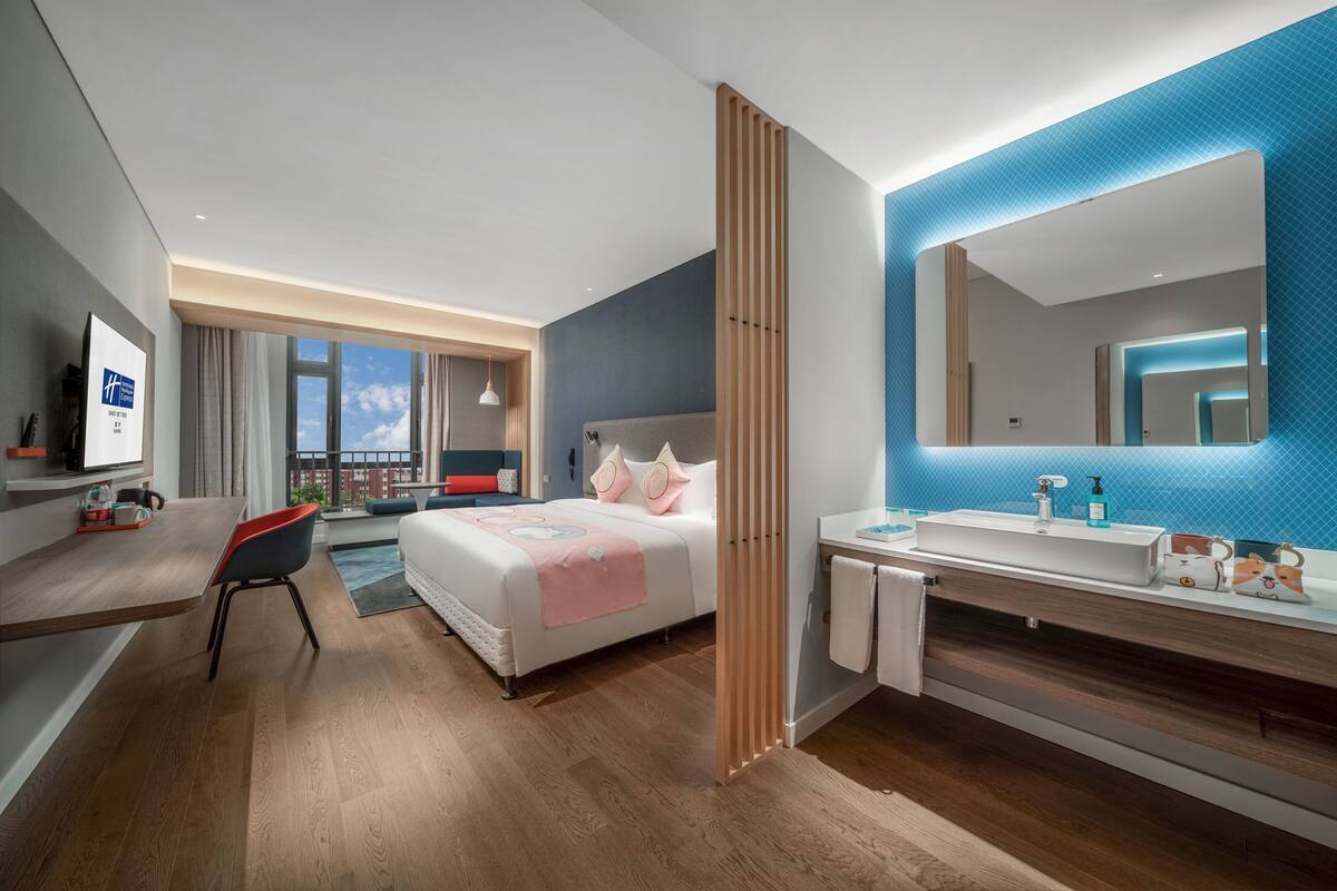 A modern hotel room with a bed, bedside table, and a large mirror.
