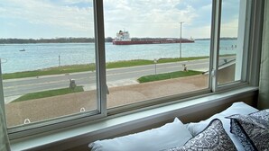 Een groot raam met uitzicht op een rivier, een schip van Canada Steamship Lines en een weg met een voetgangersoversteek.