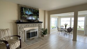 Een ruime woonkamer met een open haard, een televisie erboven en een eethoek met stoelen en een tafel.