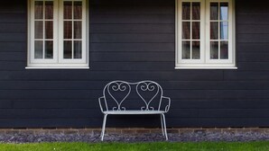 A black building with two white-framed windows and a metal bench in front. - Breckland Cottage: Secluded Country Getaway (Hockwold cum Wilton)