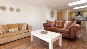 A modern living room with two sofas, a coffee table, and a kitchen in the background. - Breckland Cottage: Secluded Country Getaway (Hockwold cum Wilton)