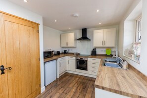 A compact kitchen with white cabinets, a wooden door, a built-in oven, and a sink. - Breckland Cottage - Secluded Country Getaway (Hockwold cum Wilton)