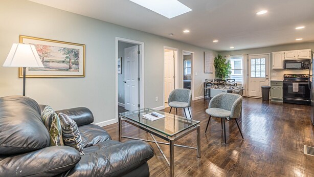 A spacious living area with a glass coffee table, leather sofa, and two armchairs. A painting is on the wall, and a skylight illuminates the room. - Welcome Home! 2BR with Driveway (Atlanta)