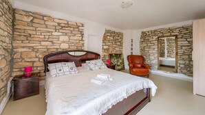 Une chambre avec un mur en pierre, un lit en bois, une chaise et un miroir.