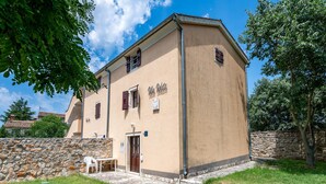 Un bâtiment à deux étages, doté d’un mur en pierre et d’une zone d’entrée pavée.