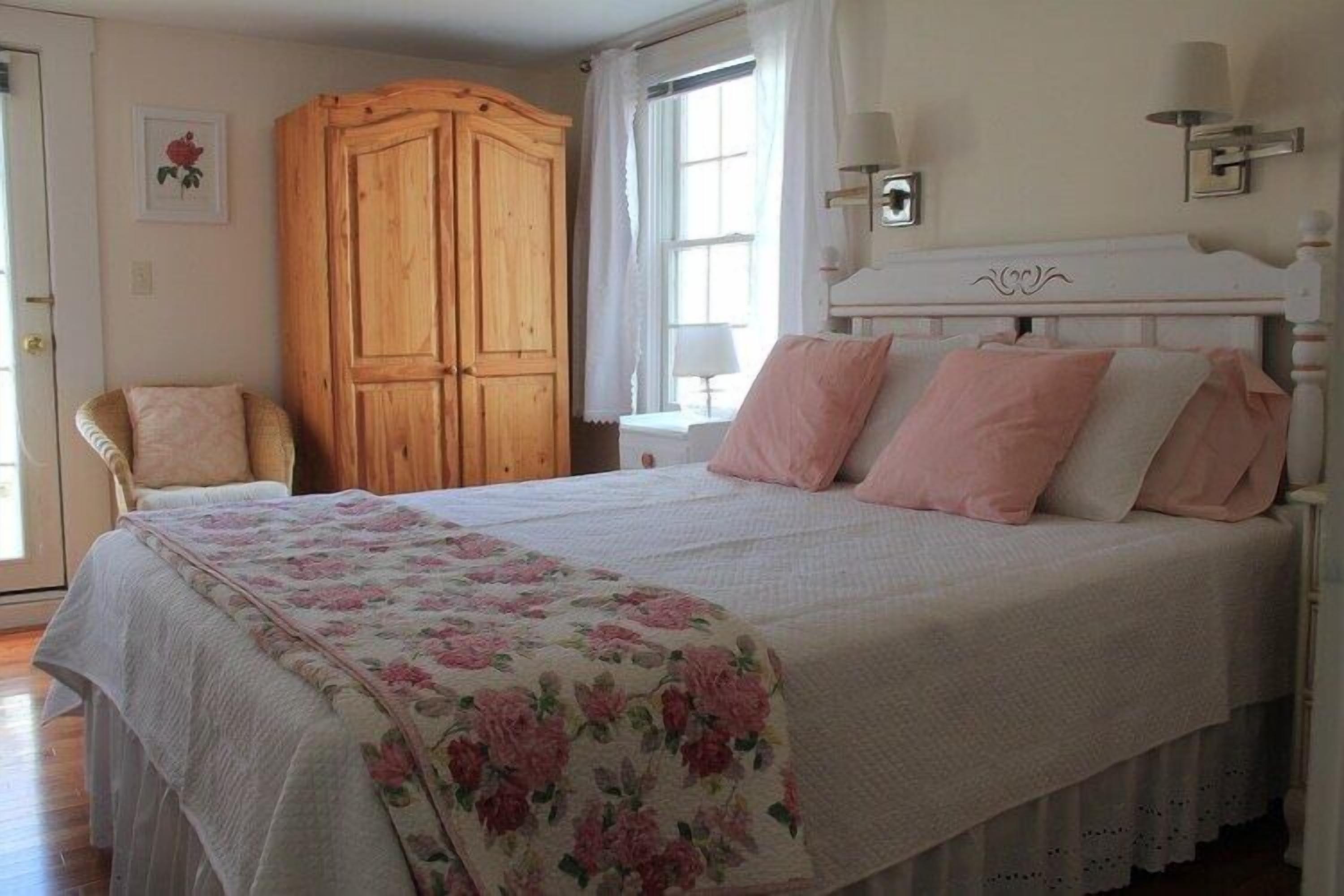 A bedroom with a large bed, a wooden wardrobe, a chair, and a window with curtains.