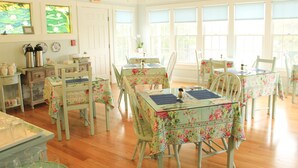 Comedor con manteles florales, sillas blancas y suelo de madera.