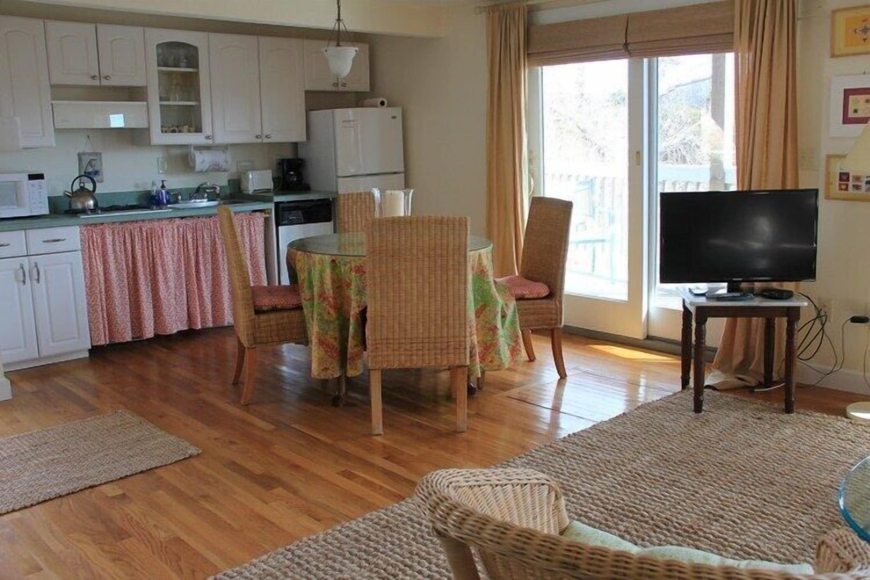 A compact living space with a kitchenette, a dining area with a table and chairs, a television, and a large window with curtains.