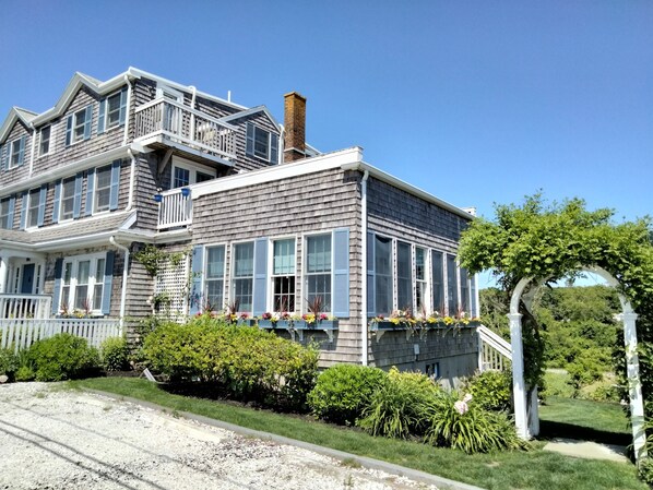 A two-story house with a balcony, a chimney, and a garden with a white archway. - An English Garden Bed & Breakfast (Dennis Port)