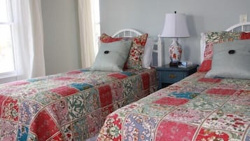 A bedroom with two beds, each with a floral-patterned bedspread and matching pillows. There is a nightstand with a lamp between the beds.