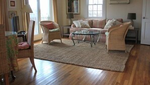 Una sala de estar con un sofá, dos sillones, una mesa de centro de vidrio y una alfombra.