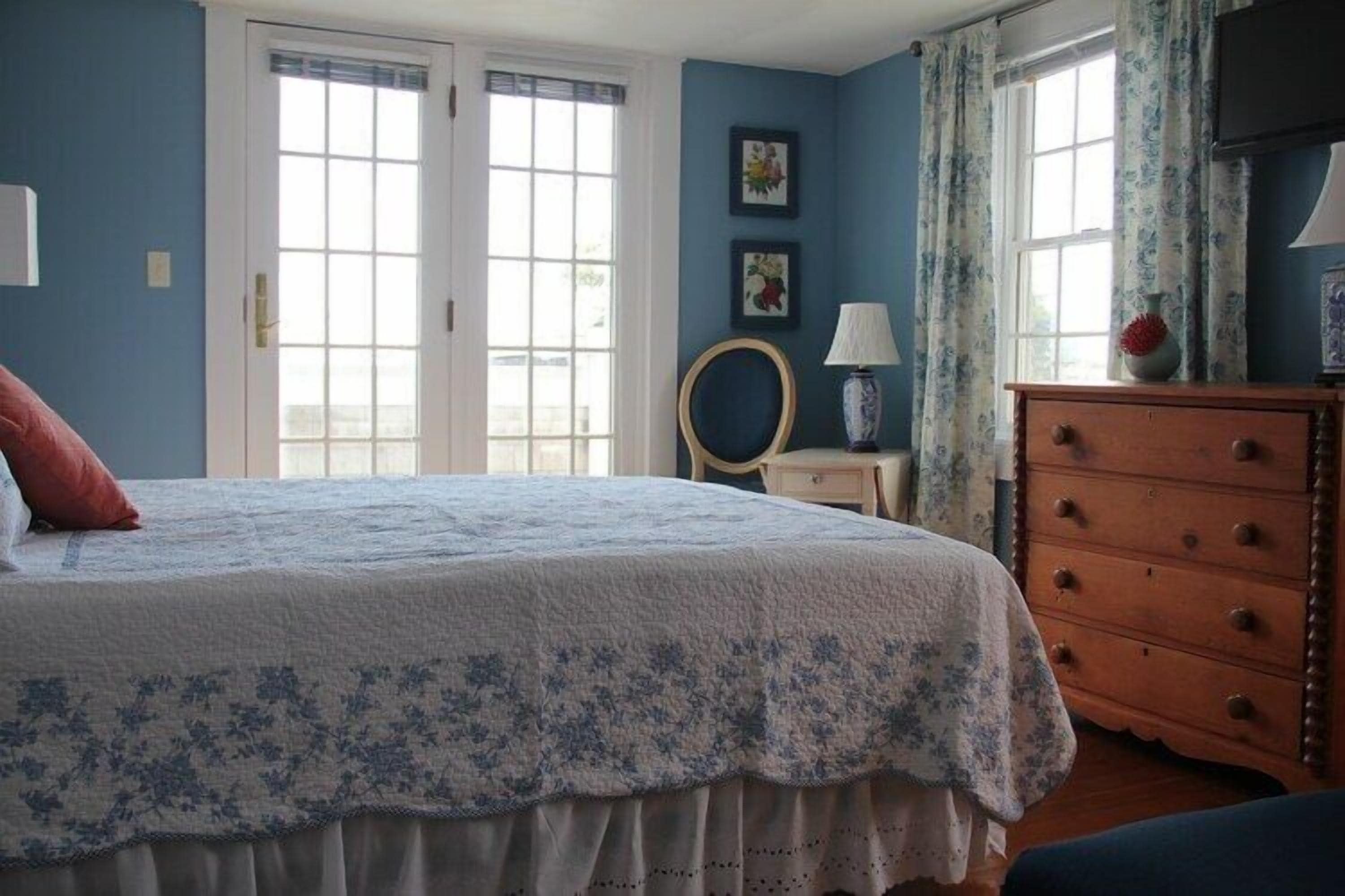 Un dormitorio con una cama grande, un aparador y dos ventanas con cortinas.