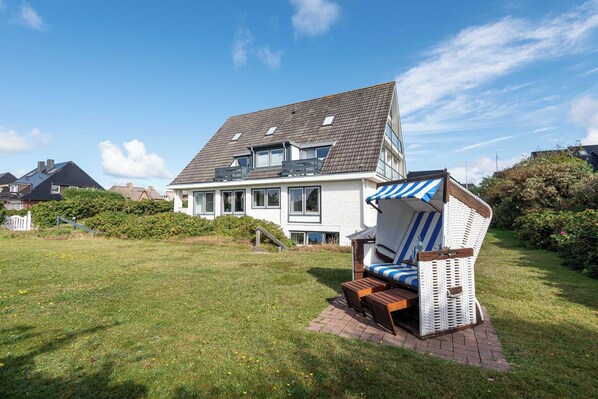 Ein zweistöckiges Haus mit großem Vorgarten, weißer Fassade und blau gestreiftem Vordach.