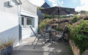 Eine Außenpatio mit Tisch und Stühlen, einem großen Sonnenschirm und Blick auf ein Gebäude mit weißer Fassade und einem Fenster.