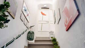 Una escalera con una puerta blanca al final, rodeada de obras enmarcadas y plantas en macetas.