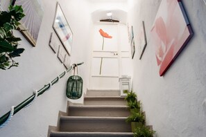 Eine Treppe mit einer weißen Tür am oberen Ende, umgeben von gerahmten Kunstwerken und Blumentöpfen.